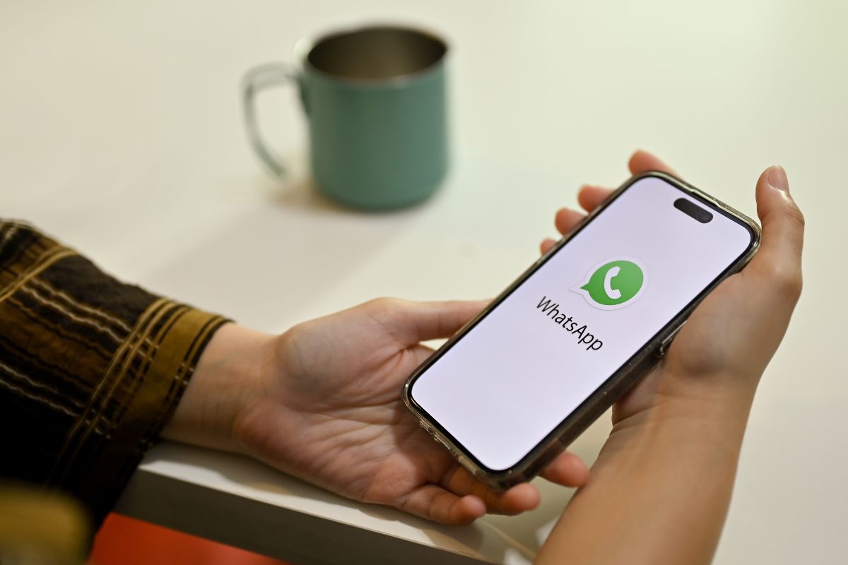 Main tenant un smartphone affichant l'écran de démarrage de WhatsApp.